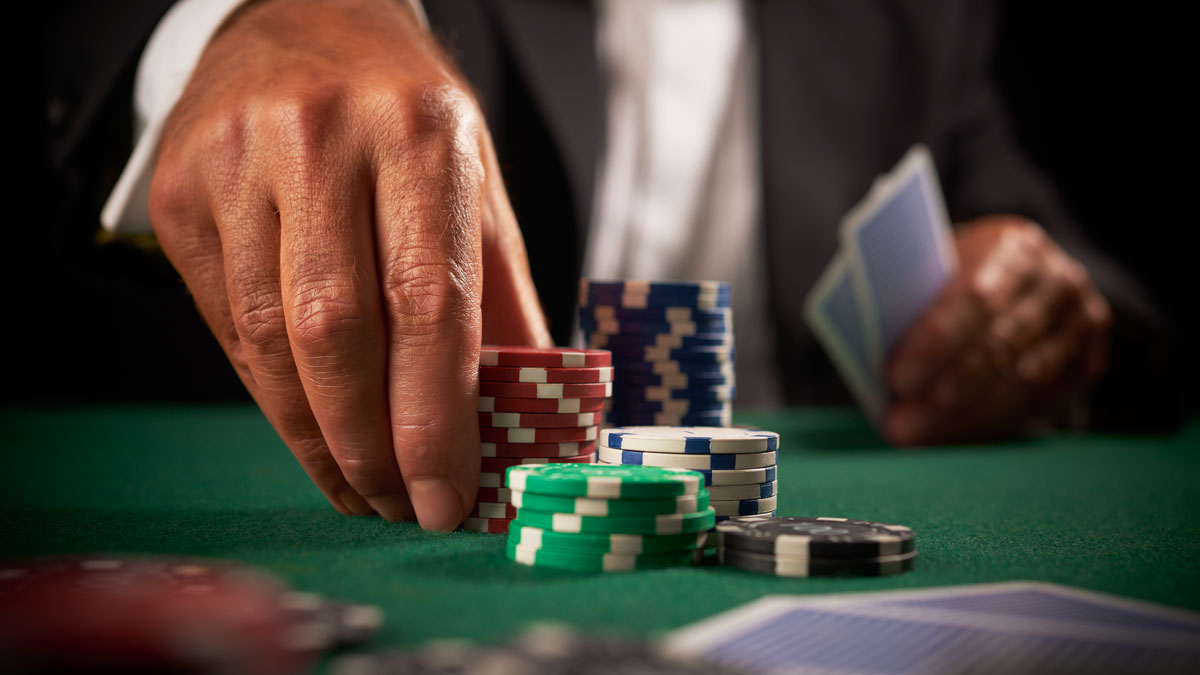 A Man Holding Two Cards With A Hand on One of the Chip Stacks on the Green Felt Table